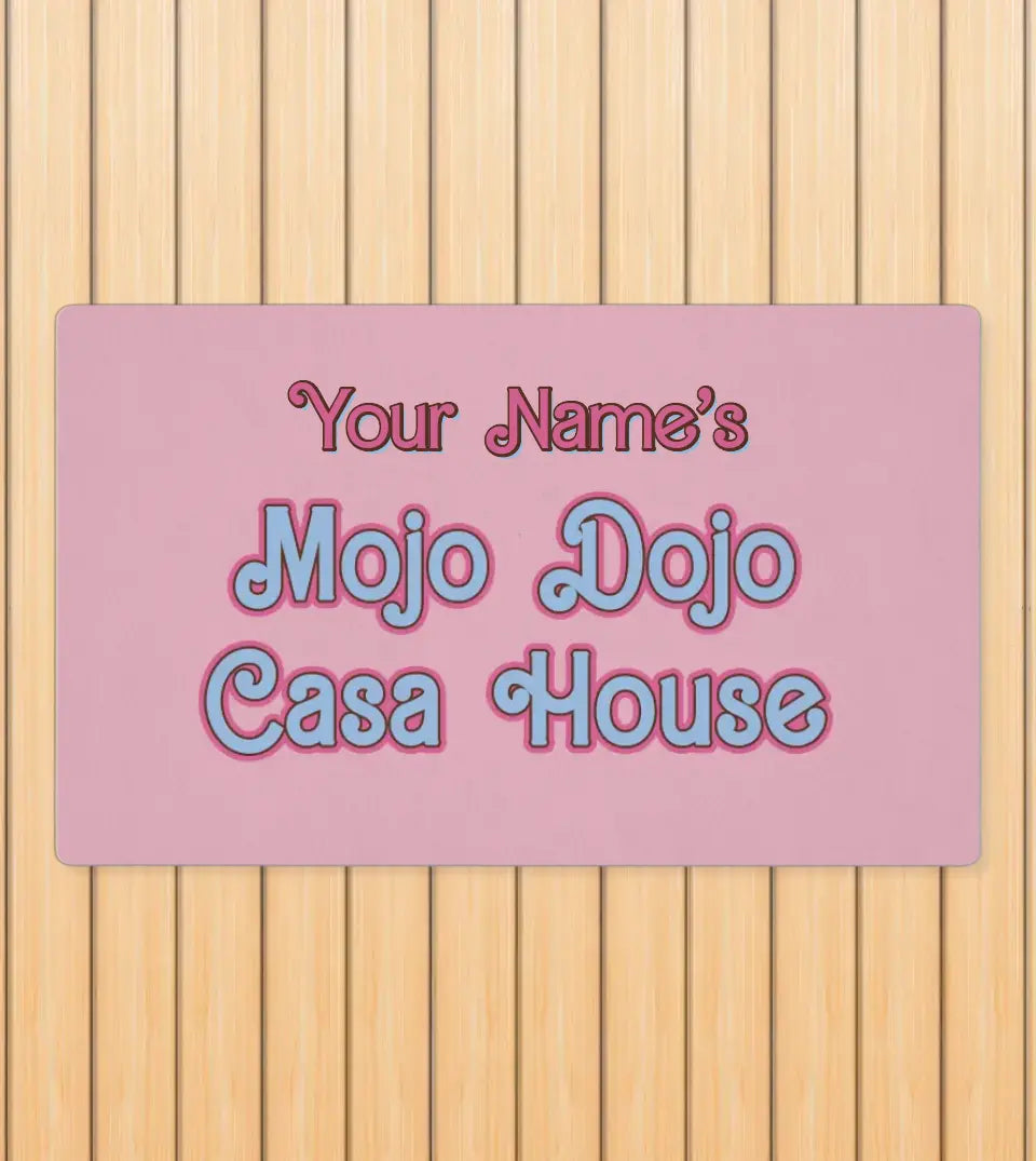 Pastel pink doormat with 'Mojo Dojo Casa House' text, horseshoe design, and space for a custom family name, embodying a Barbiecore aesthetic.