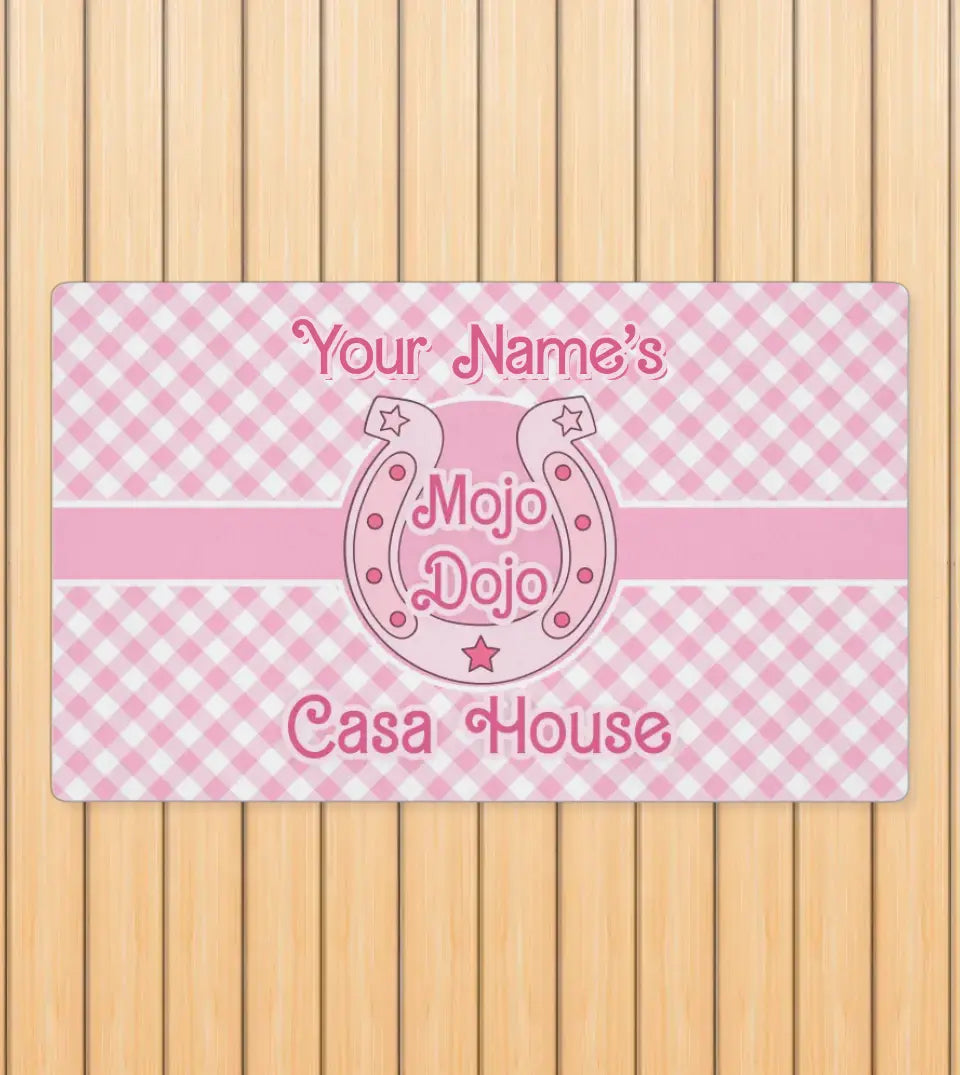 Pastel pink plaid doormat with 'Mojo Dojo Casa House' text and customizable family name, designed in a Barbiecore style, displayed against a neutral background
