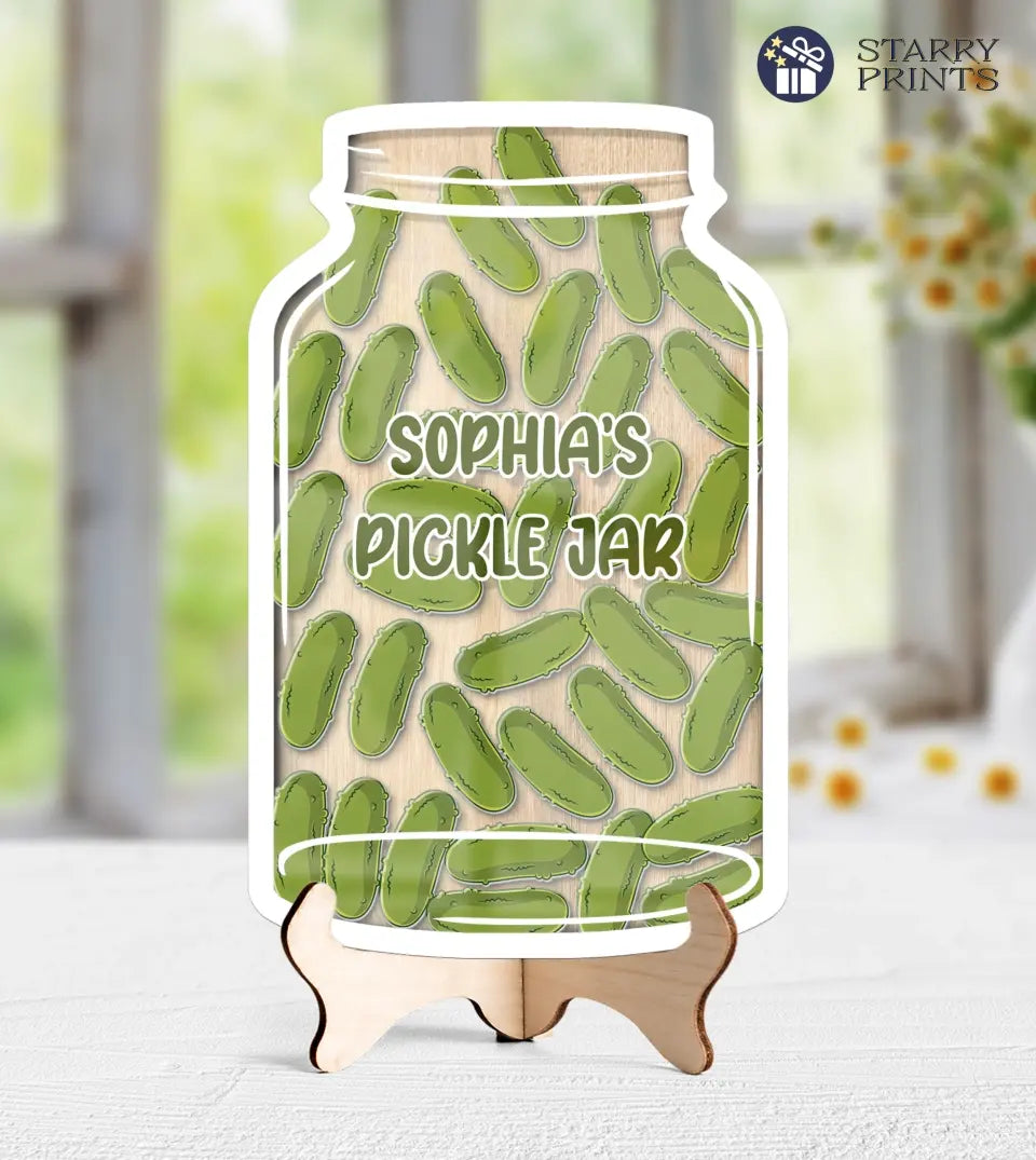 A clear acrylic reward jar filled with green pickle-shaped tokens, set against a white background. The jar showcases a customizable label, and the tokens inside serve as markers for achievements or goals met.