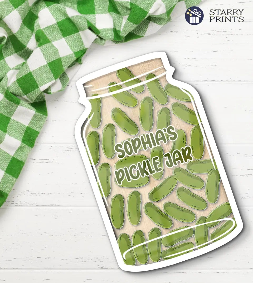 A clear acrylic reward jar filled with green pickle-shaped tokens, set against a white background. The jar showcases a customizable label, and the tokens inside serve as markers for achievements or goals met.