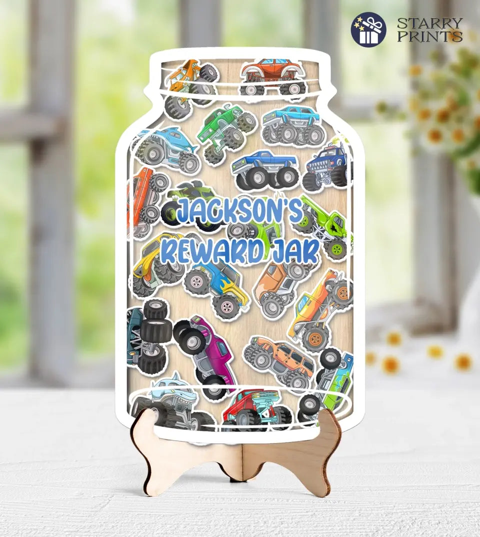 Clear acrylic reward jar filled with vibrant monster truck tokens, showcasing a customizable nameplate at the front. The jar is accompanied by a rustic wooden stand, emphasizing its premium quality and detailed design