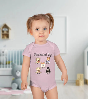 A Baby girl wearing a pink baby onesie with a quote "Protected by" followed by a portrait of a dog or cat and their name printed on it.
