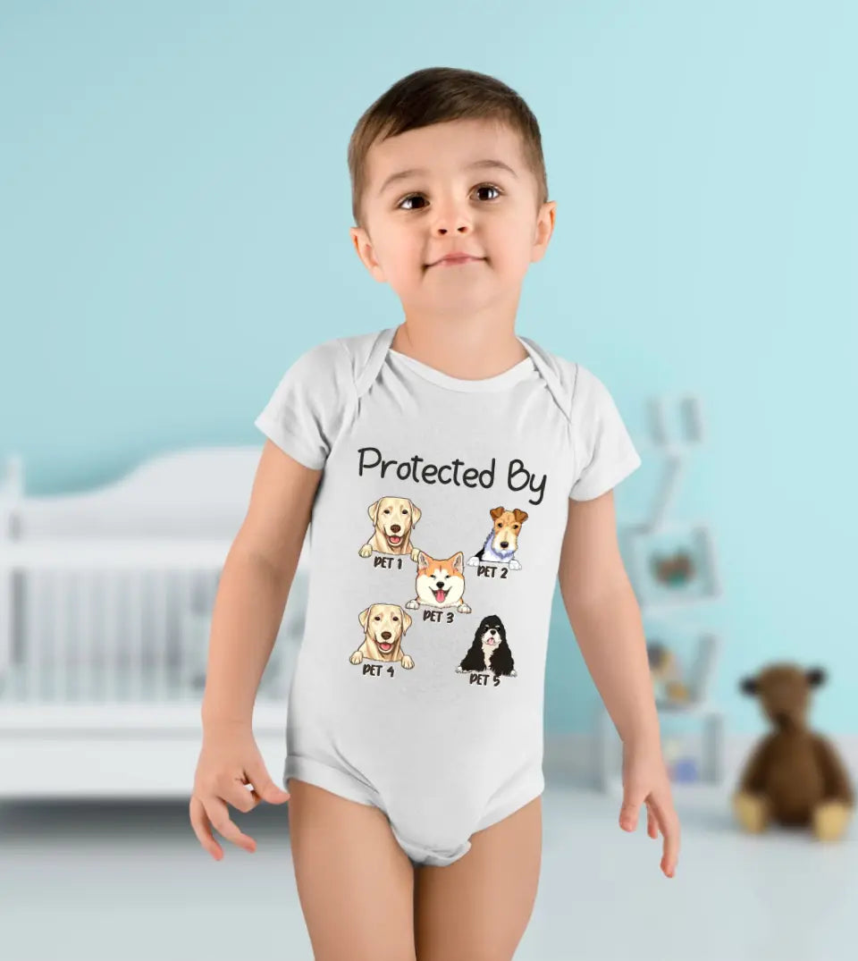 A Baby boy wearing a white baby onesie with a quote "Protected by" followed by a portrait of a dog or cat and their name printed on it.