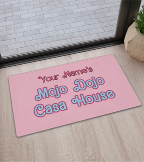 Pastel pink doormat with 'Mojo Dojo Casa House' text, horseshoe design, and space for a custom family name, embodying a Barbiecore aesthetic.