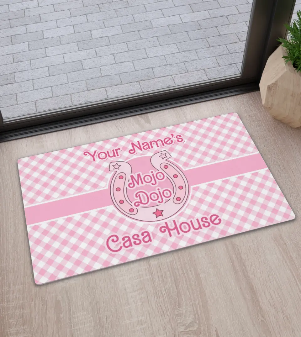 Pastel pink plaid doormat with 'Mojo Dojo Casa House' text and customizable family name, designed in a Barbiecore style, displayed against a neutral background